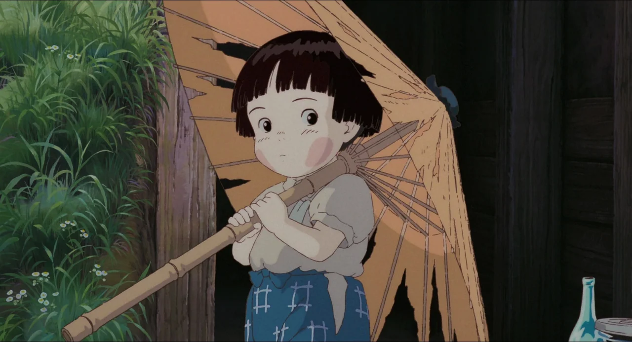 Grave of the Fireflies (1988) movie still: medium — A small child stands beside a rustic structure overgrown with tall green grasses. She holds a…