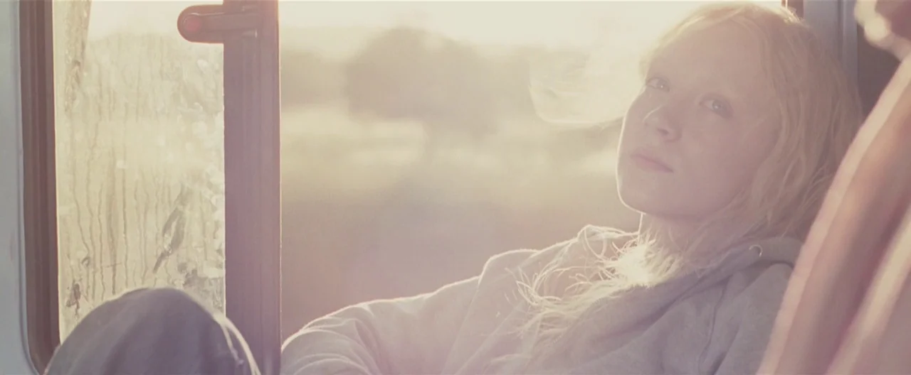 Hanna (2011) movie still: medium — A passenger sits on a bus near a window during the late afternoon. Sunlight fills the frame, washing out the…