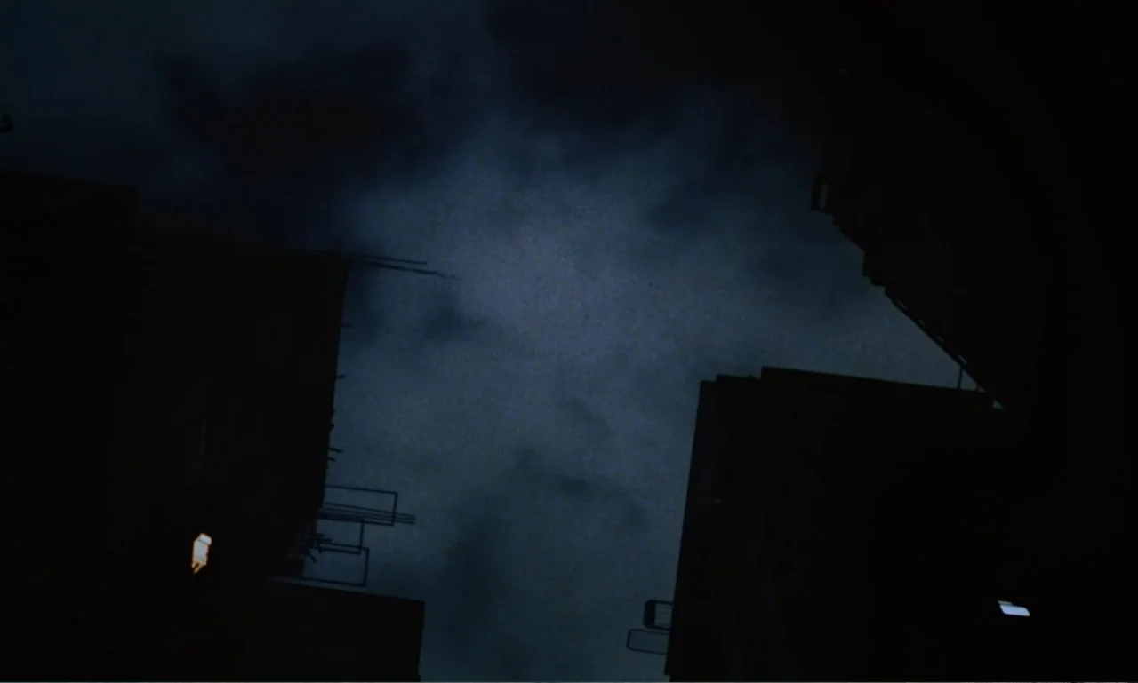 Chungking Express (1994) movie still: establishing — Dark silhouettes of tall buildings frame a view of a cloudy night sky. A small illuminated…