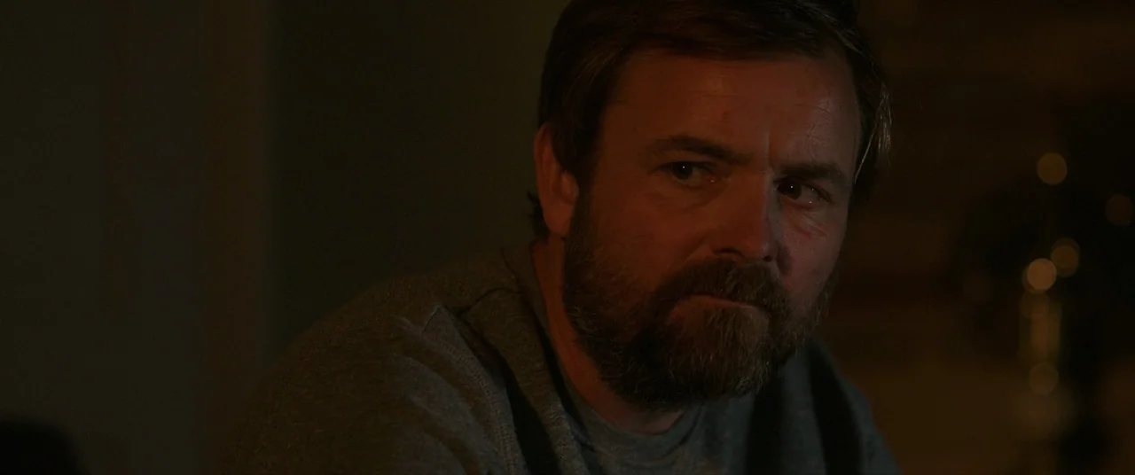 Bull (2021) movie still: closeup — A dimly lit room provides minimal detail of the surrounding environment at night. A middle-aged man with a full…