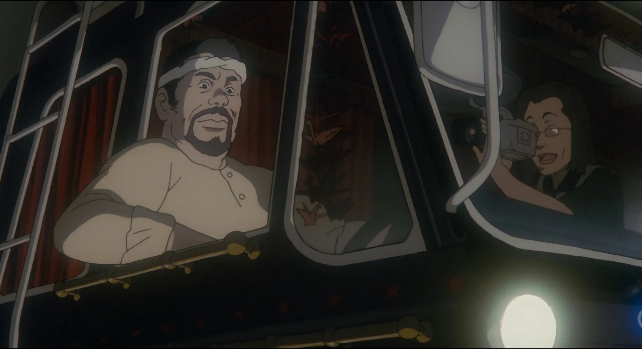 Millenium Actress (2001) movie still: medium — The interior of a large truck cab at night with red curtains. The male driver looks ahead while the…