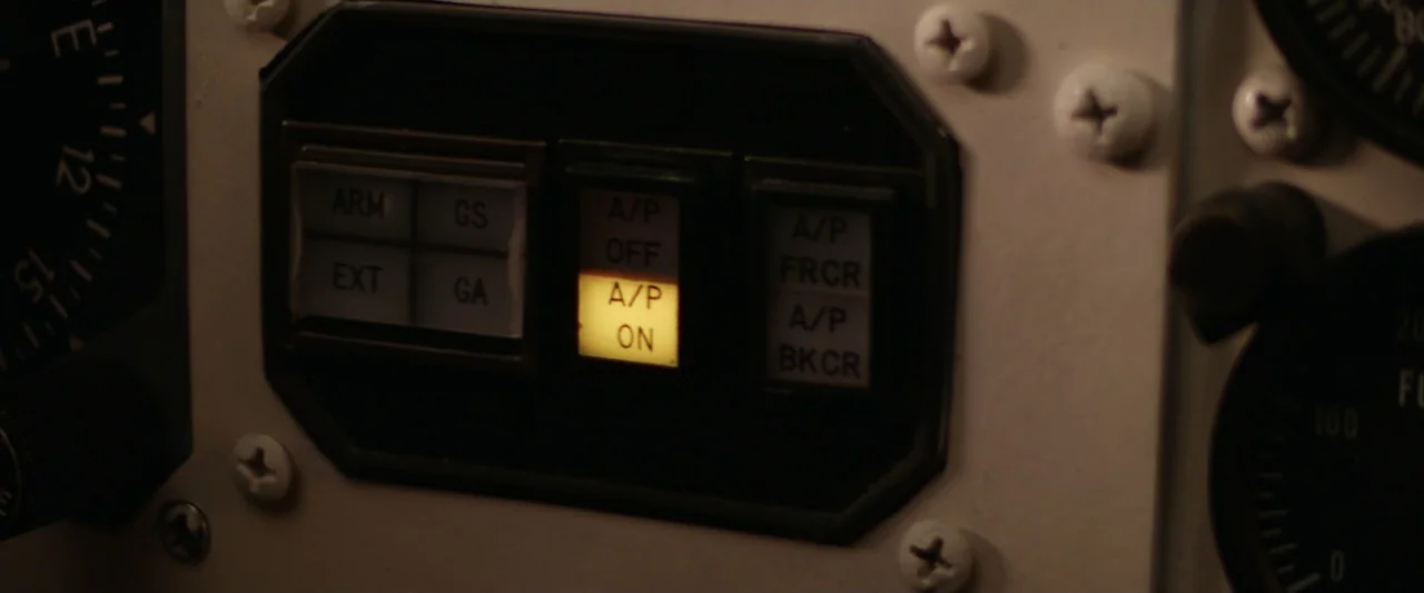 On a Wing and a Prayer (2023) movie still: closeup — A close-up view of an airplane control panel with various labeled buttons. One switch labeled…