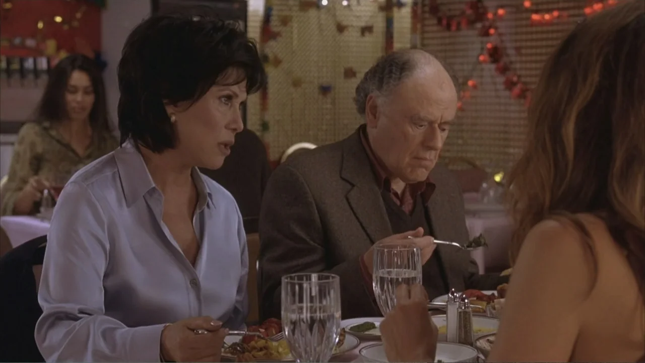 Along Came Polly (2004) movie still: medium — A restaurant dining area features white tablecloths and festive red decorations in the background. A…