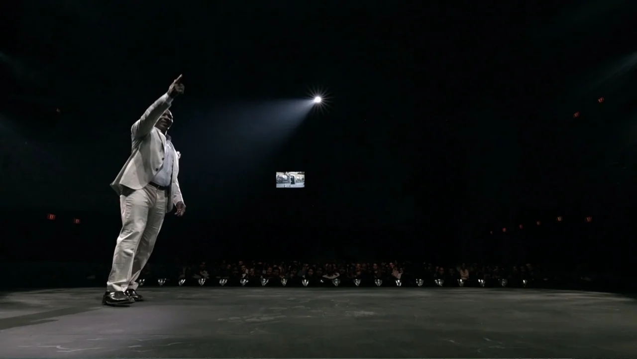 Mike Tyson: Undisputed Truth (2013) movie still: fullbody — A man in a light suit stands alone on a dark, expansive stage floor. A single bright…