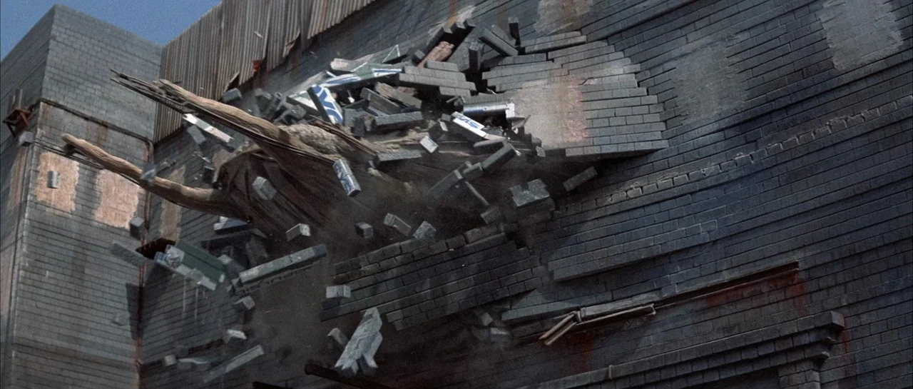 The Adventures of Buckaroo Banzai Across the 8th Dimension (1984) movie still: wide — An industrial brick building wall is shattering outward as a…