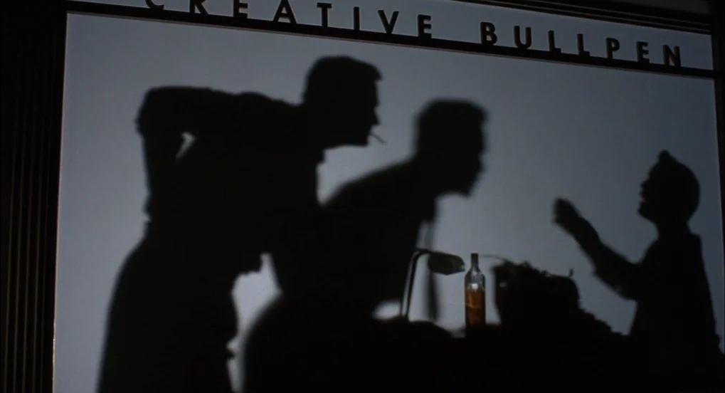 The Hudsucker Proxy (1994) movie still: medium — A frosted glass partition features the words Creative Bullpen painted in bold black letters. Three…