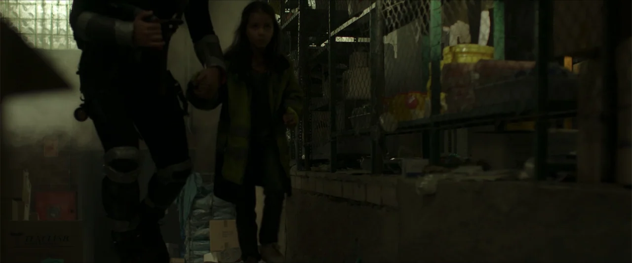 Apocalypse Z: The Beginning of the End (2024) movie still: medium — A dark indoor storage space features metal shelving units behind a chain link…
