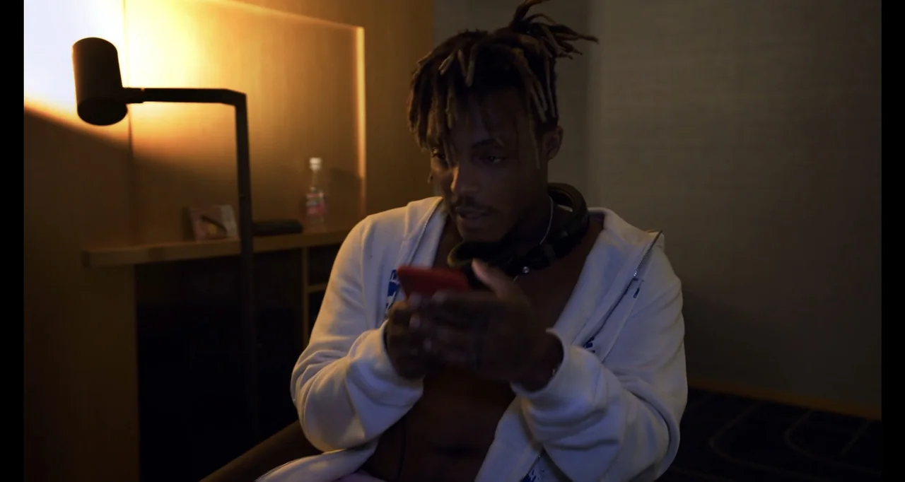 Juice WRLD: Into the Abyss (2021) movie still: medium — A dark hotel room interior contains a lamp and a man holding a phone. The man sits alone…