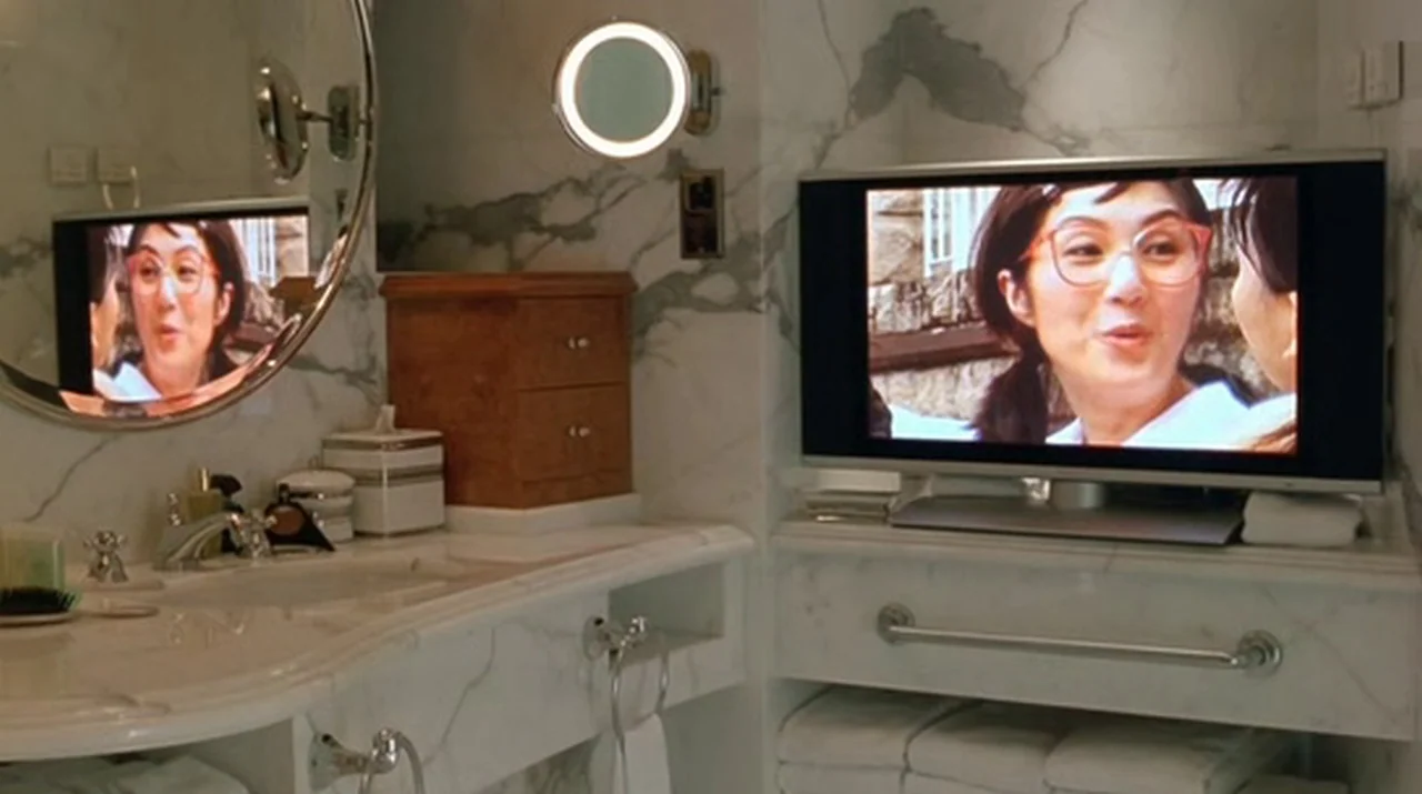 Dumplings (2004) movie still: wide — A luxury hotel bathroom features white marble countertops, a round mirror, and a television. The television…