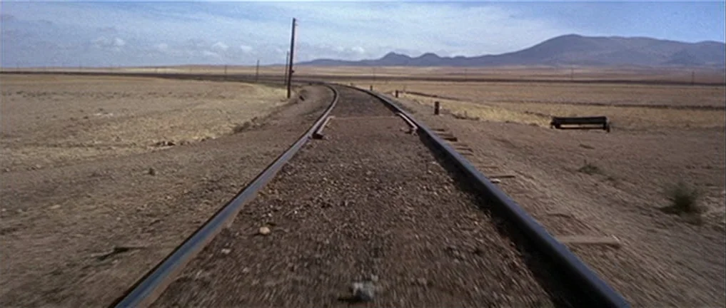 The Good, The Bad And The Ugly (1966) movie still: establishing — A desolate desert landscape features a single set of train tracks curving slightly…