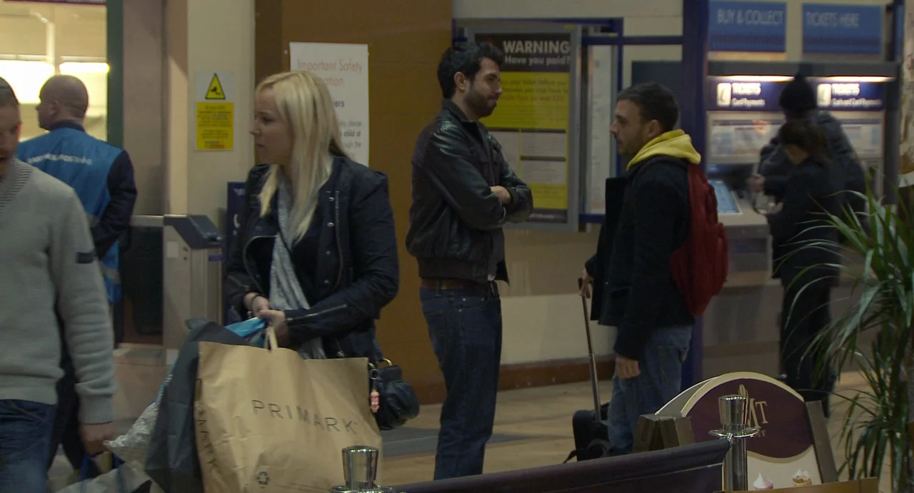 Weekend (2011) movie still: medium — A public transport concourse features ticketing machines, safety signage, and a small potted plant. Three…