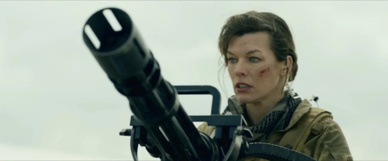 Monster Hunter (2020) movie still: medium — An outdoor desolate area serves as the setting under a grey overcast sky. A woman with a facial injury…