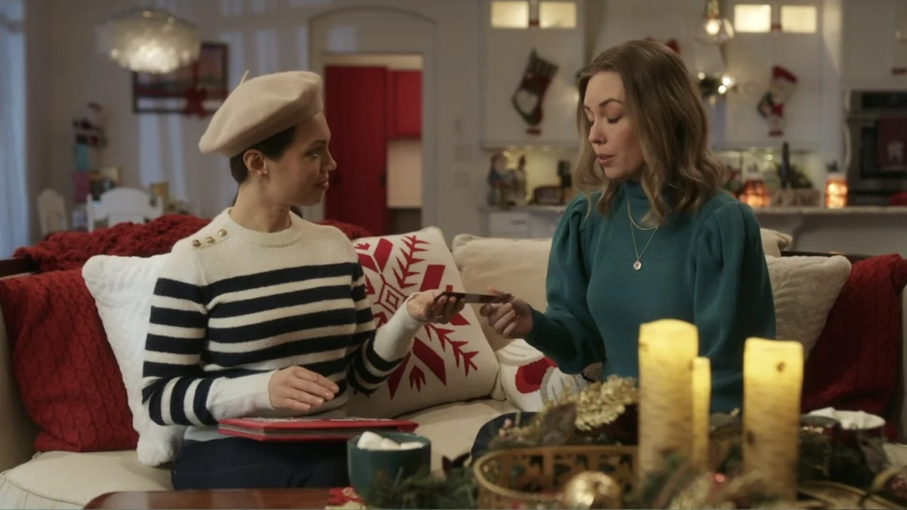 Peppermint and Postcards (2023) movie still: medium — A cozy living room is decorated for the holidays with stockings and candles visible. Two women…