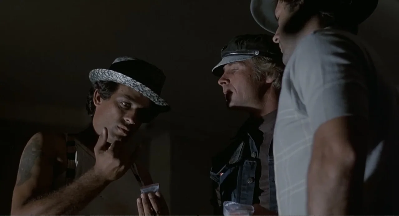 Death Wish II (1982) movie still: medium — Three men stand inside a dimly lit space in a dark room. One man examines a small clear plastic bag while…