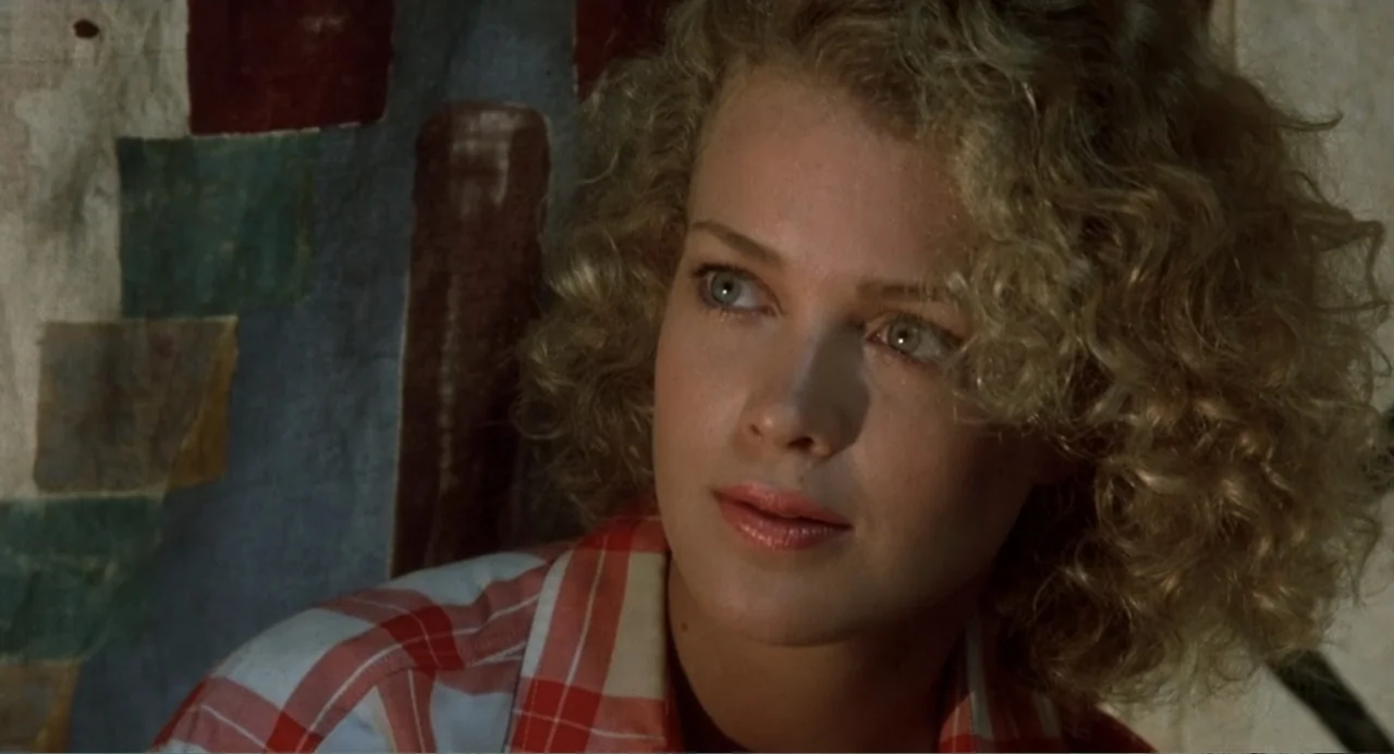 Firewalker (1986) movie still: closeup — A woman sits in a room with a patterned fabric wall hanging behind her. She looks toward the side while…