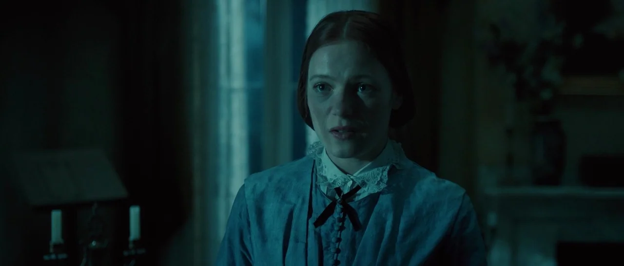 A Quiet Passion (2016) movie still: medium — A dimly lit room with blue-tinted shadows and traditional 19th-century decor visible in background. A…