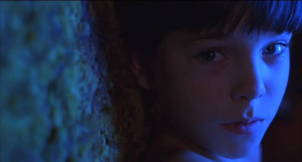 Mysterious Skin (2004) movie still: closeup — A dark space features a boy positioned next to a coarse, textured wall. The boy gazes directly ahead…