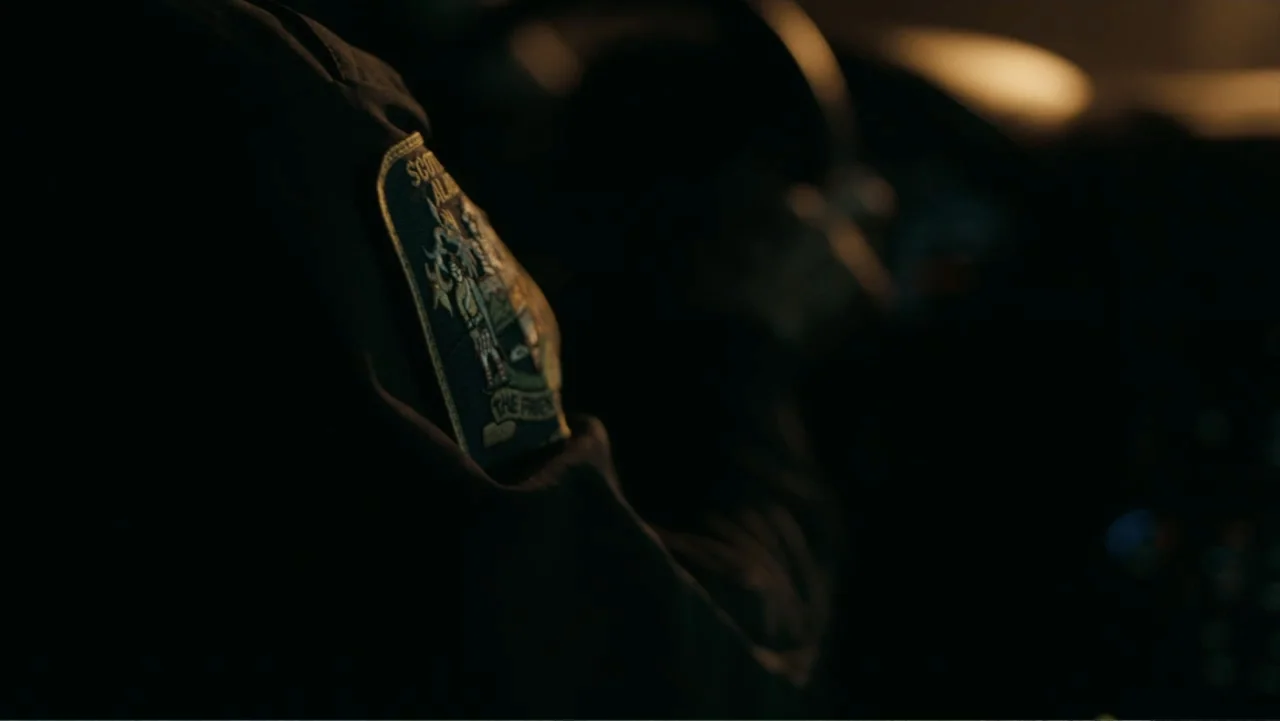Alabama Snake (2020) movie still: closeup — The interior of a vehicle at night featuring a dark sleeve and shoulder patch. A person sits at the…