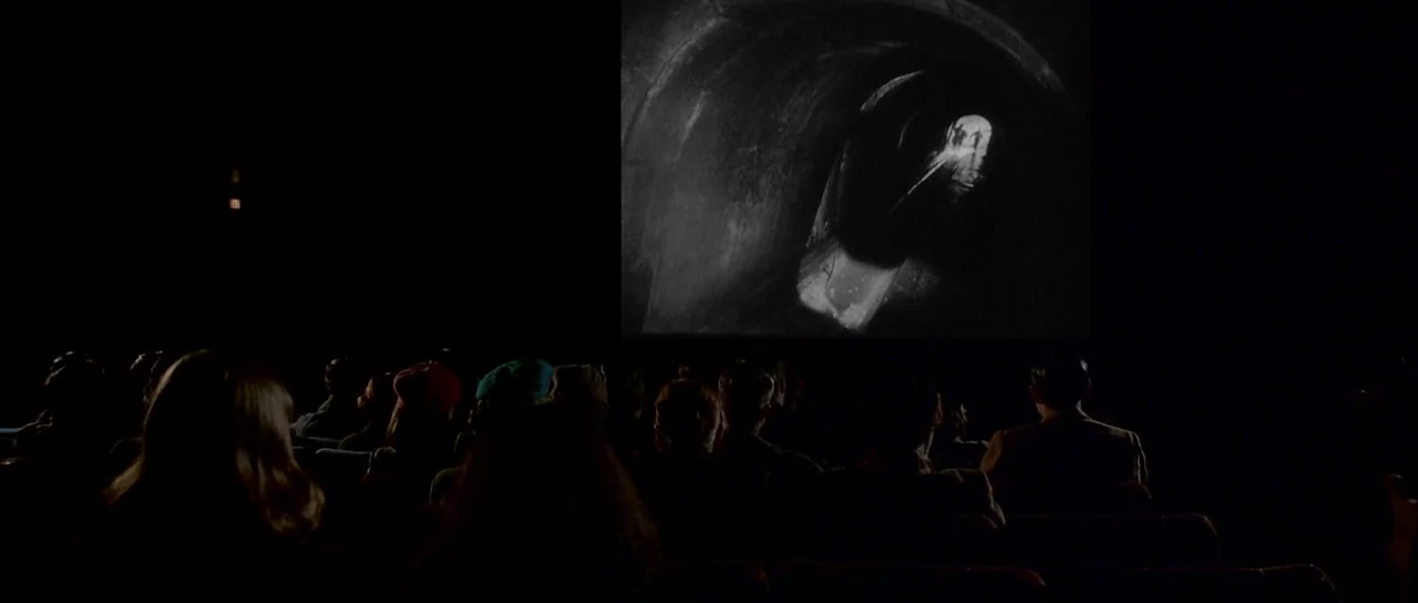 Heavenly Creatures (1994) movie still: wide — A dark movie theater auditorium features an audience seated in rows facing a screen. A black and white…