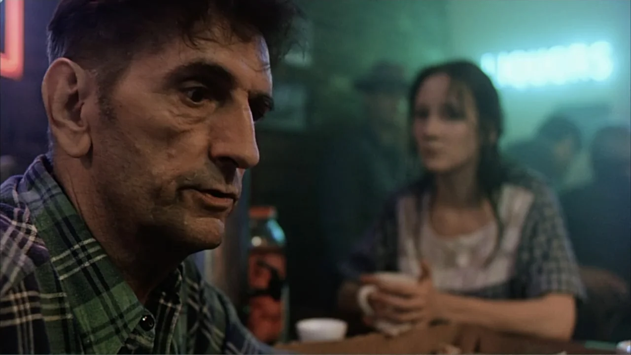 Against the Wall (1994) movie still: medium — A dark, dimly lit bar features a neon sign in the background near a wall. A man in a flannel shirt…