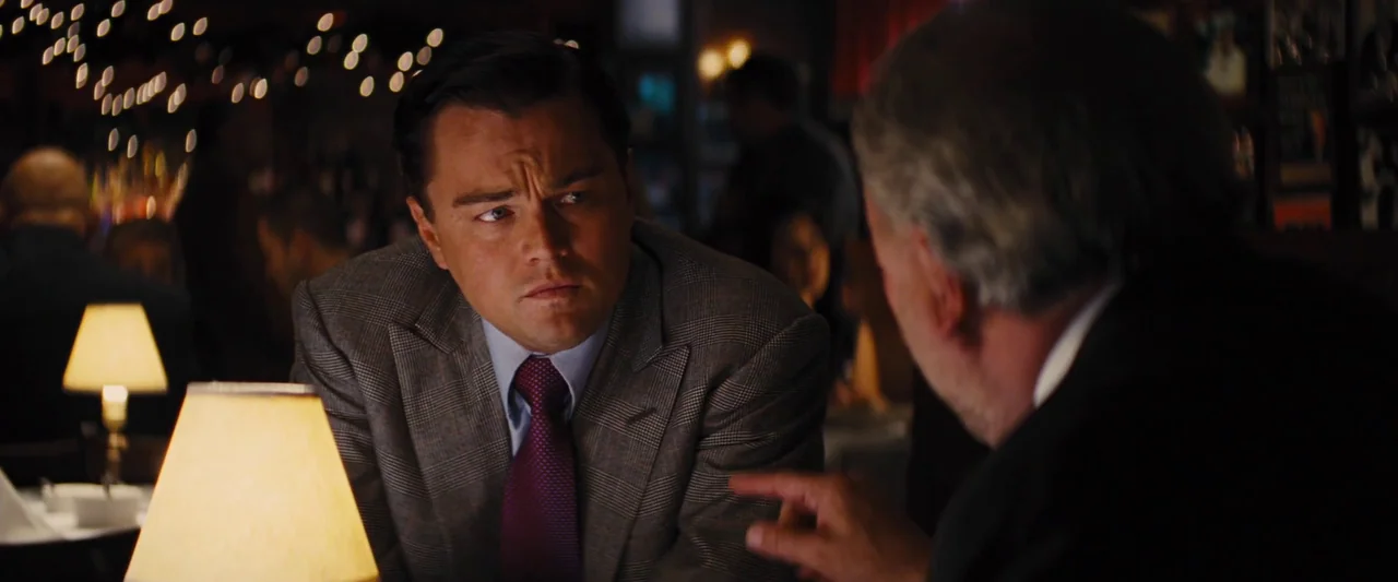 The Wolf of Wall Street (2013) movie still: medium — A dimly lit restaurant interior features blurred background lights and dark wood panels. Two…