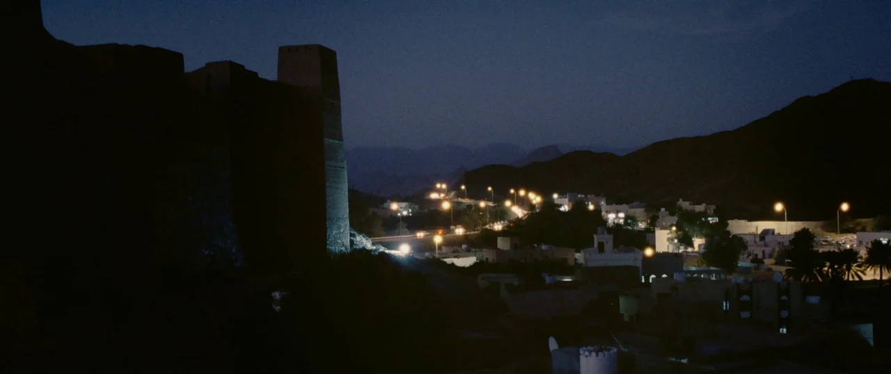 Personal Shopper (2016) movie still: establishing — A dark ancient stone fort stands prominently against a vast desert valley at night. Rows of…