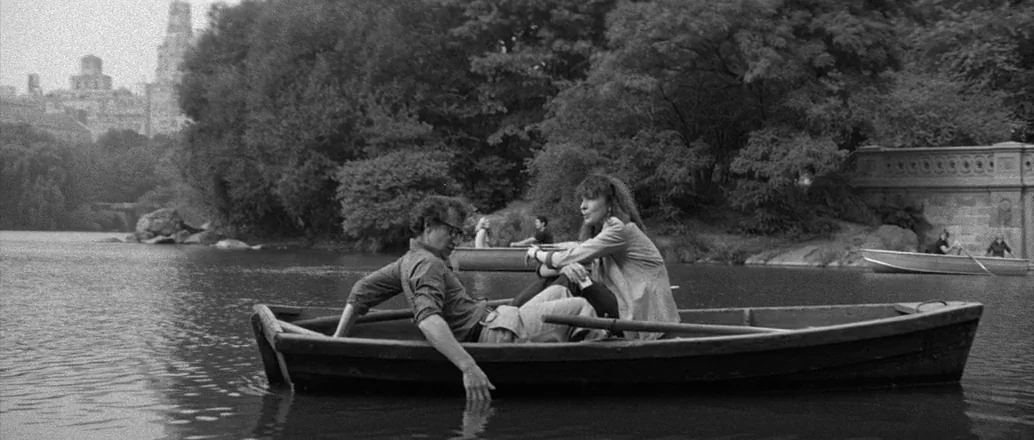 Manhattan (1979) movie still: wide — A man and woman sit in a wooden rowboat on a calm park lake. Dense trees and a distant stone bridge frame the…