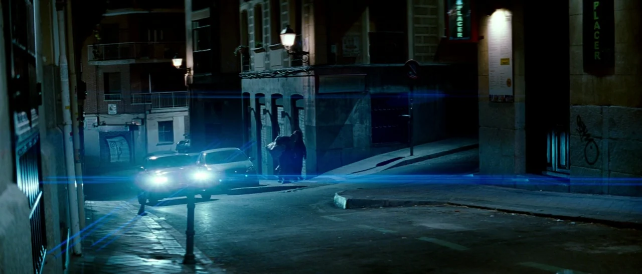 Broken Embraces (2009) movie still: wide — A dark, narrow urban intersection at night features illuminated streetlamps and nearby apartment…