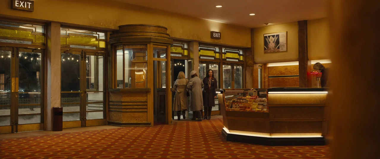 Empire of Light (2022) movie still: wide — A 1940s-style theater lobby features Art Deco architecture, red patterned carpet, and wooden ticket…
