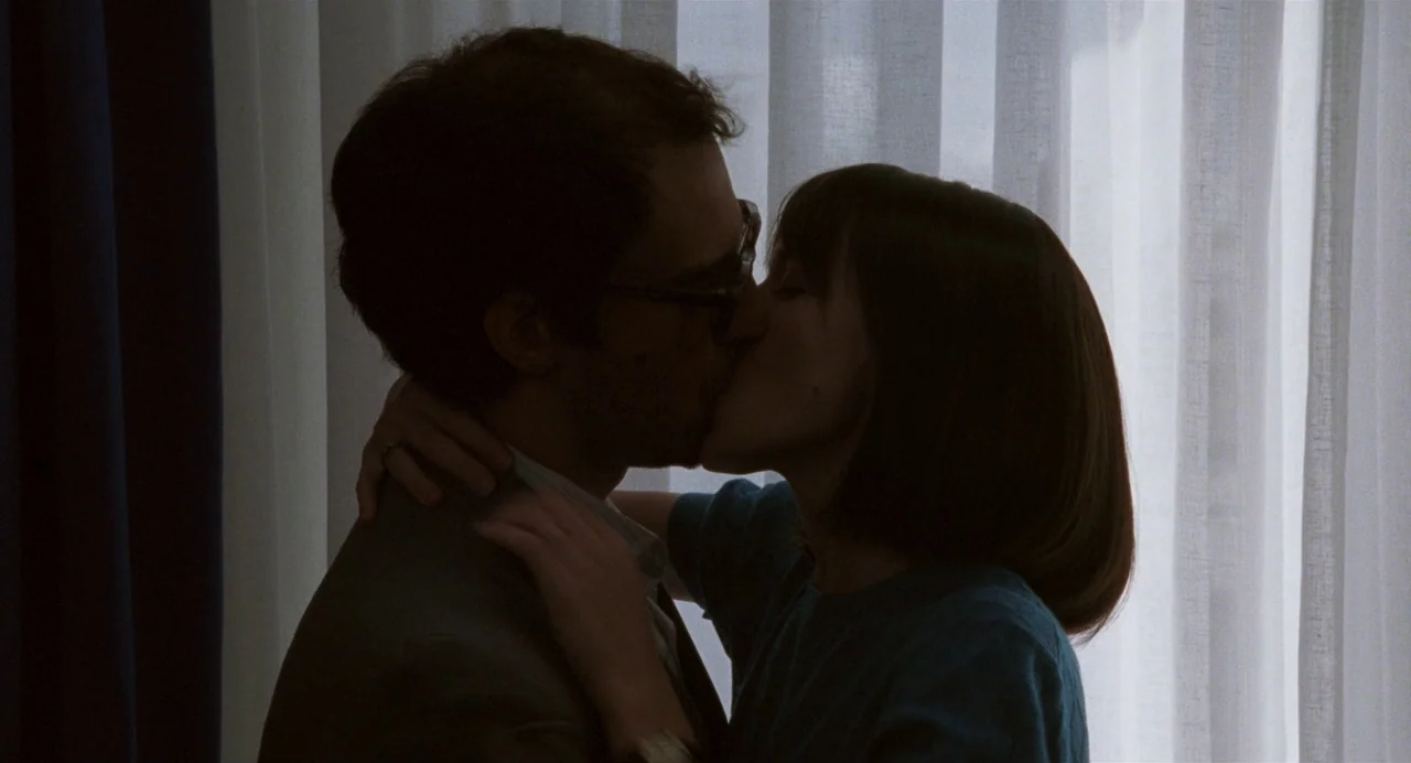 Godard Mon Amour (2015) movie still: medium — A man and woman embrace in front of thin, translucent white curtains.
