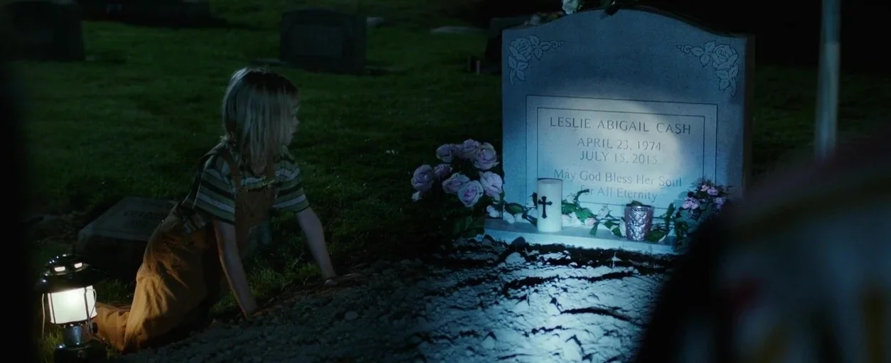 Captain Fantastic (2016) movie still: medium — A dark cemetery at night features an illuminated granite grave marker among grass. A young girl in…