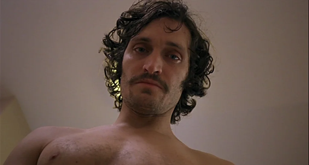 Trouble Every Day (2001) movie still: closeup — A man is viewed from a low angle against a plain, off-white ceiling. He hovers over the lens while…