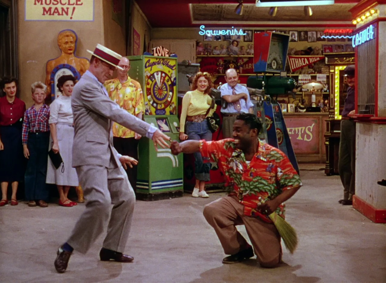 The Band Wagon (1953) movie still: fullbody — An indoor arcade with vintage coin-operated gaming machines and colorful neon signage. A man in a suit…