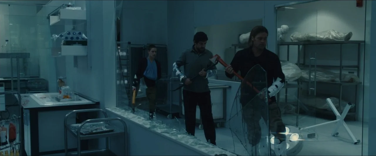 World War Z (2013) movie still: fullbody — A sterile hospital laboratory contains metal shelving units and large glass partition walls. Three men…