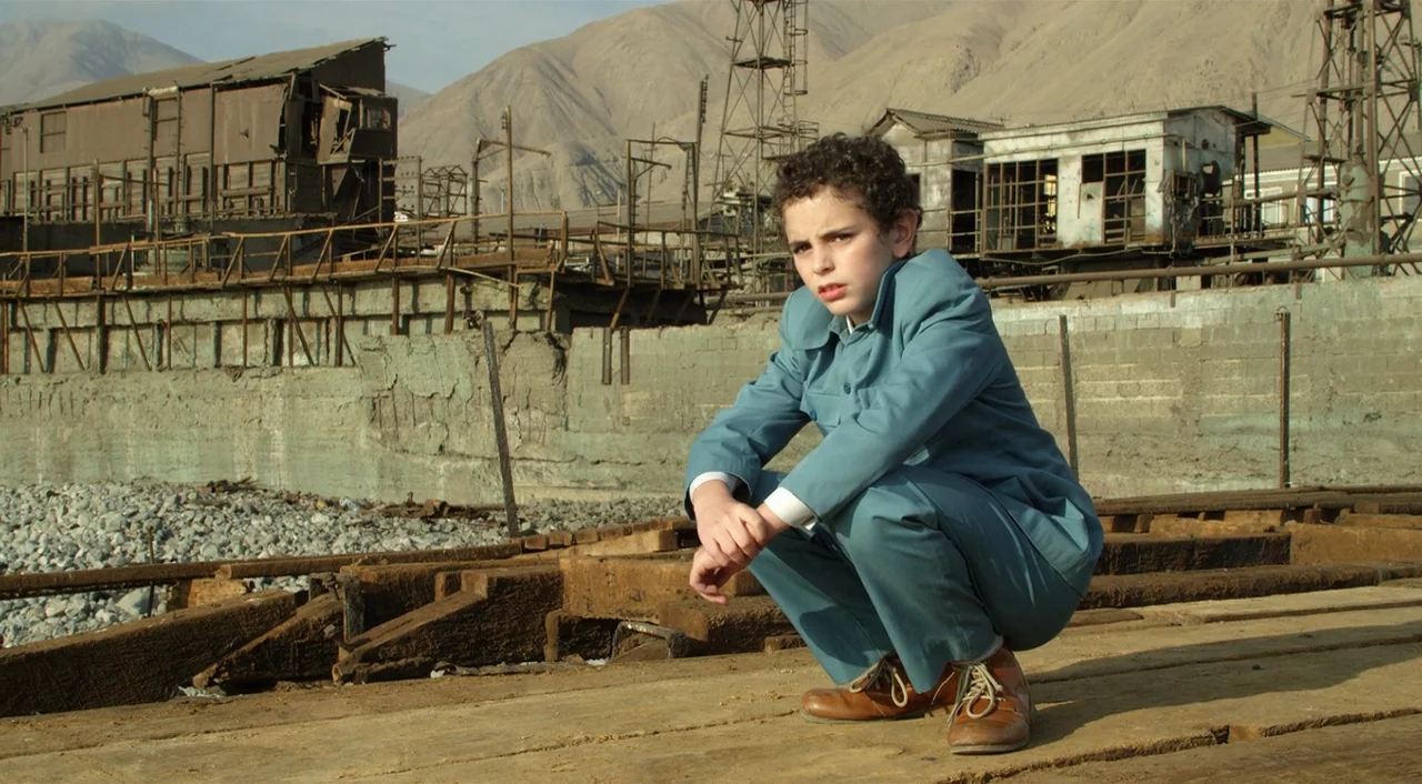 Dance of Reality (2013) movie still: medium — A desolate industrial shipyard with rusted metal structures and gravel sits against barren mountains.…