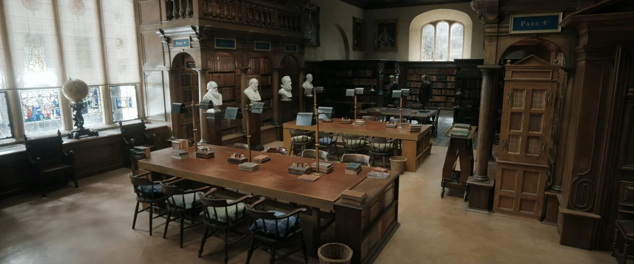 Young Sherlock Holmes (1985) movie still: wide — A spacious academic library with dark wood paneling, multiple long reading tables, and busts. The…