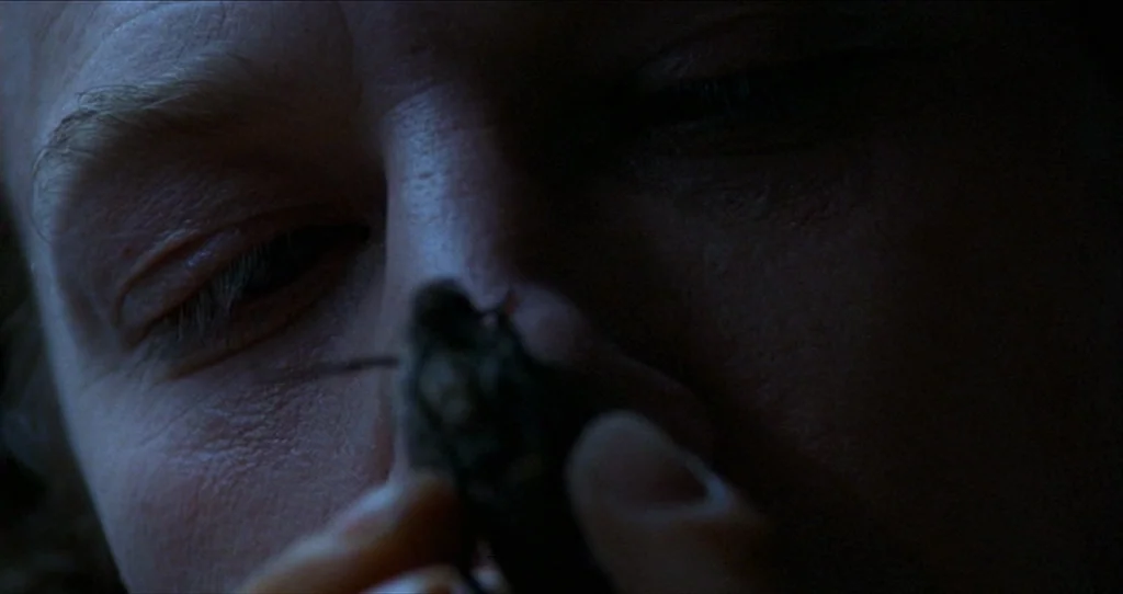 The Silence Of The Lambs (1991) movie still: closeup — A close-up shot focuses on a person's face held in deep shadow. A person holds a small…