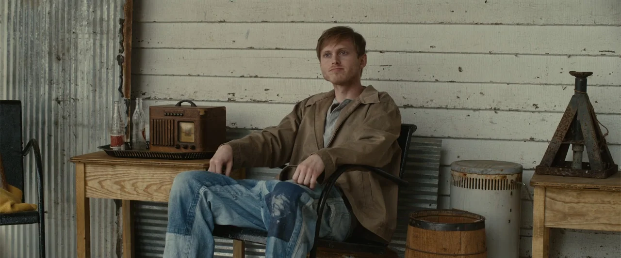 Coming Through the Rye (2016) movie still: medium — A wooden porch with white horizontal siding and various vintage props including a radio. A young…