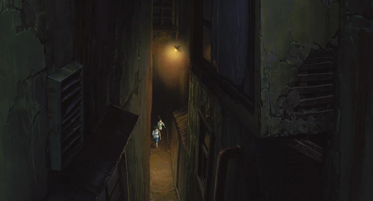 Spirited Away (2001) movie still: wide — A narrow, dark city alleyway with weathered building walls and an overhead lamp. Two young characters walk…