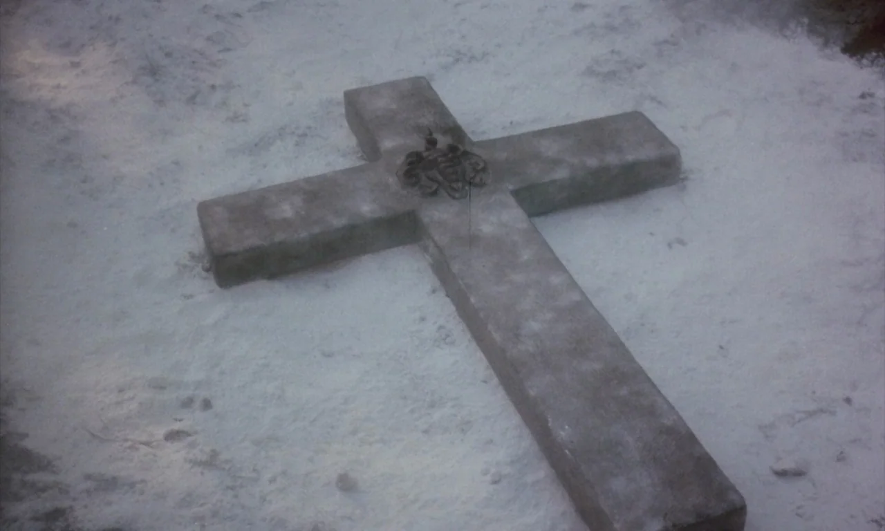 The Church (1989) movie still: closeup — A stone cross lies embedded in a flat, snow-covered surface of a grave. The structure is weathered and…