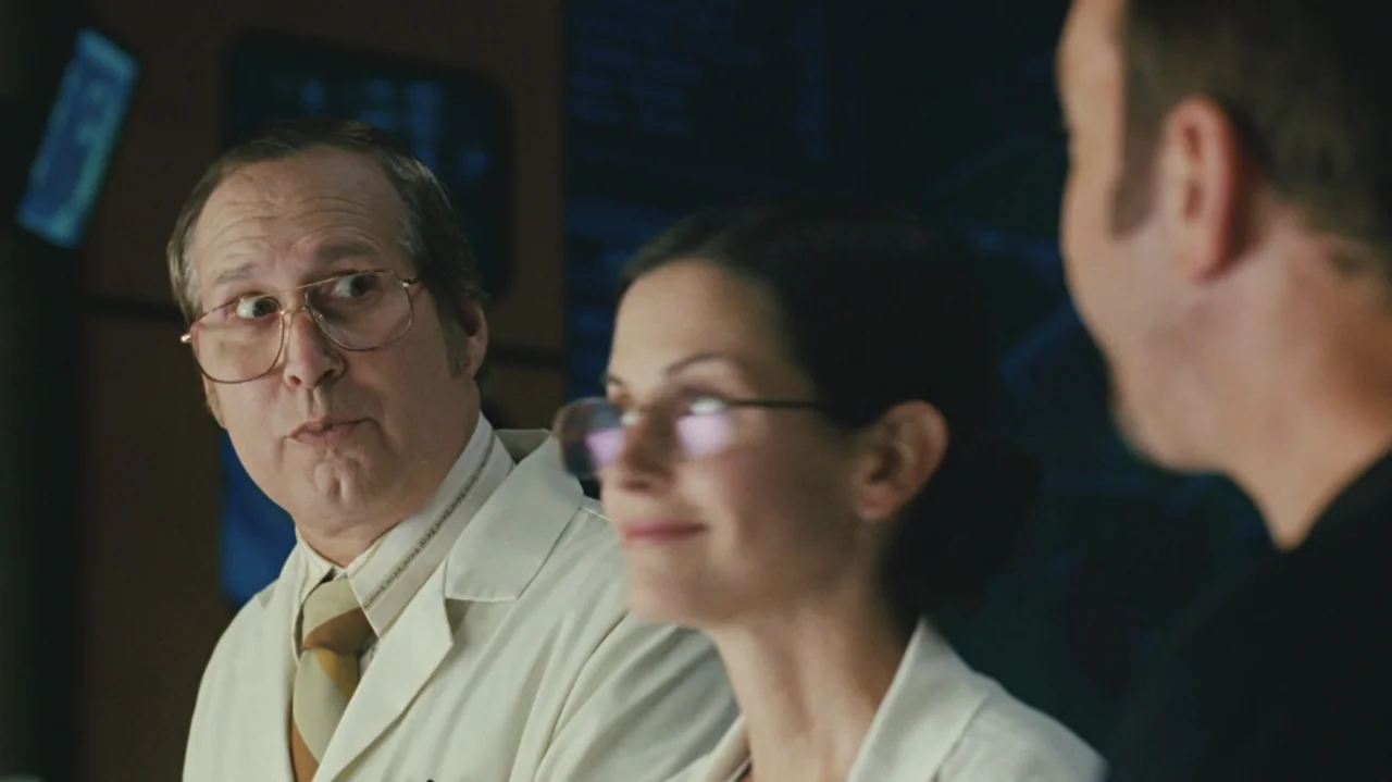 Zoom (2006) movie still: medium — A sterile laboratory setting features three people standing together in front of digital displays. The man in the…