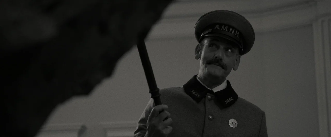 Wonderstruck (2017) movie still: medium — A dimly lit museum interior features white walls and shadowed exhibits. A night guard in a grey uniform…