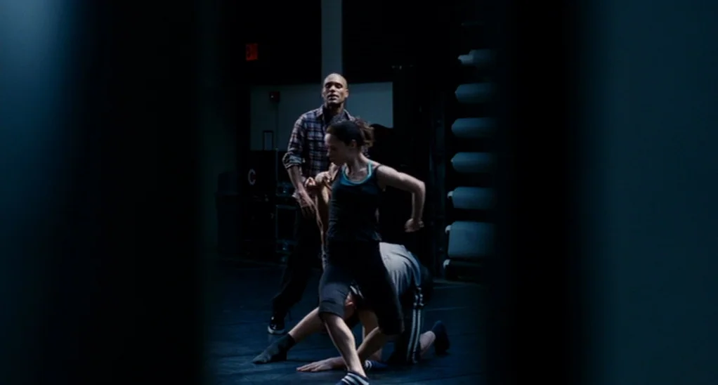 The Adjustment Bureau (2013) movie still: medium — A dark, sparsely furnished dance practice space features black floors and stacked equipment. A…