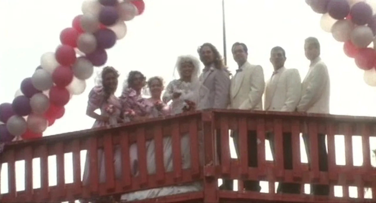 The Annihilation of Fish (1999) movie still: fullbody — A group of people stands on a wooden balcony decorated with balloon arches. The bride and…