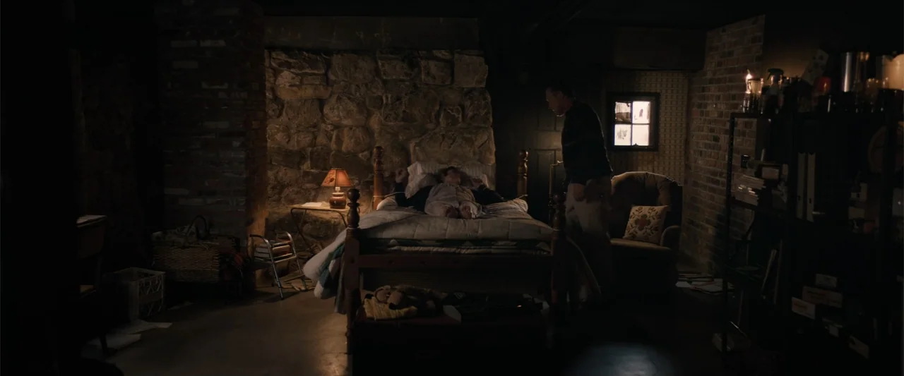 Equation of Love and Tone Deafness (2015) movie still: wide — A basement room features stone walls and brick supports with sparse furnishings. A man…