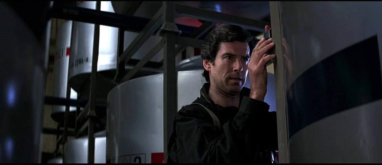 GoldenEye (1995) movie still: medium — An industrial facility features large metallic storage tanks arranged in rows under dim light. A man in black…