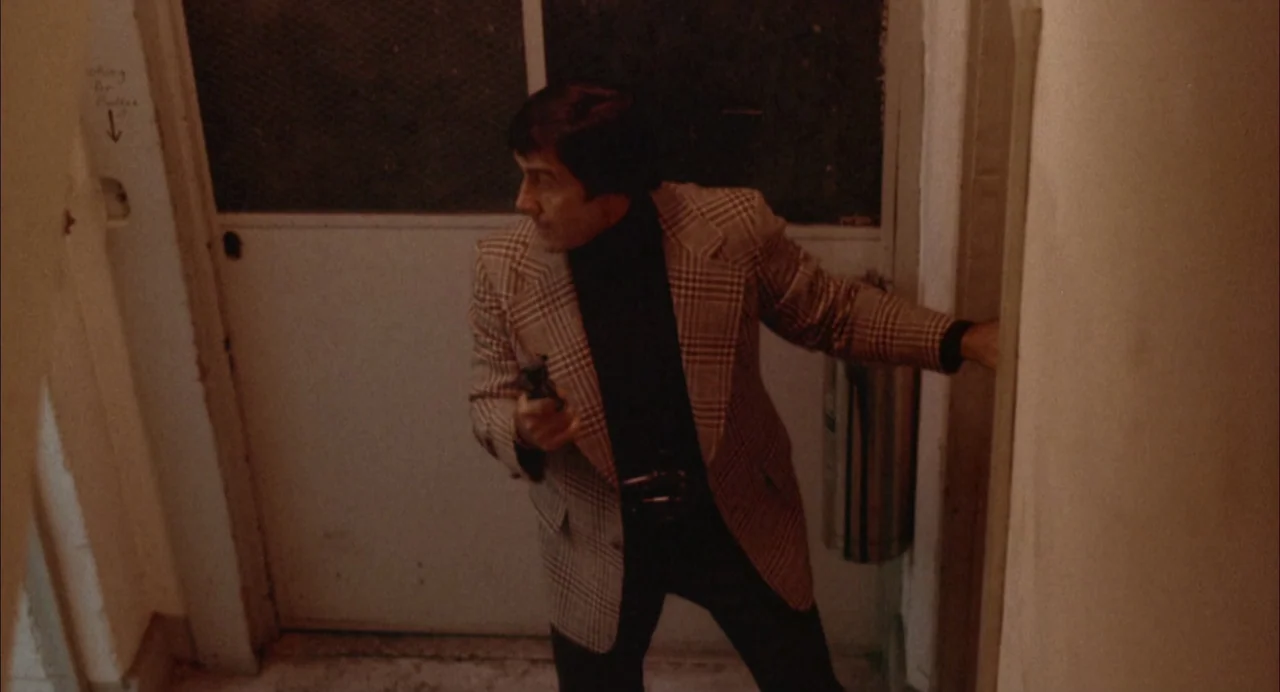 The Killing of a Chinese Bookie (1976) movie still: medium — A utilitarian stairwell interior features a metal door and a wall-mounted fire…
