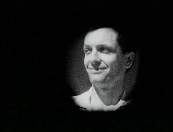 Cowards Bend The Knee (2003) movie still: closeup — A man's head and shoulders are framed within a circular vignette. The subject gazes towards the…