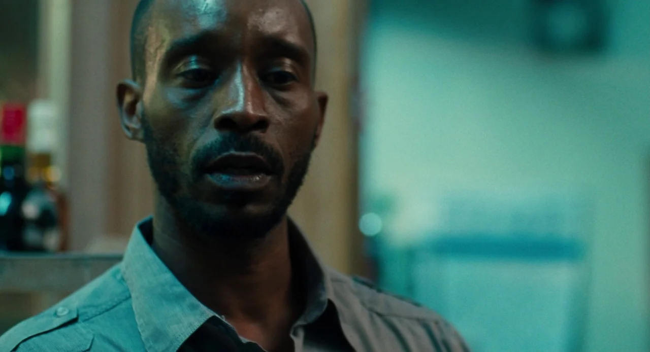 Pariah (2011) movie still: closeup — A dimly lit room with cool teal ambient light highlighting a man's face. The man stands looking forward with a…