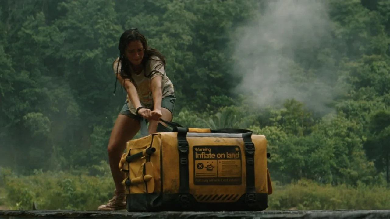 Jurassic World Rebirth (2025) movie still: medium — A wooden dock sits before a dense, mist-covered green jungle background. A woman in casual…